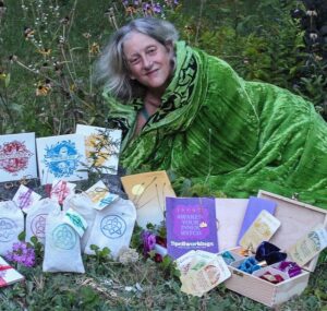 Annie Finch in a green cloak lying on the grass among her poetry books, stationery, and herbal teas