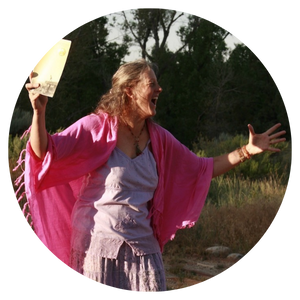 Annie Finch outisde in front of trees in a pink shawl and purple dress,hwith both arms outstretched passionately, olding a book of poetry in one hand, seeming to be chanting